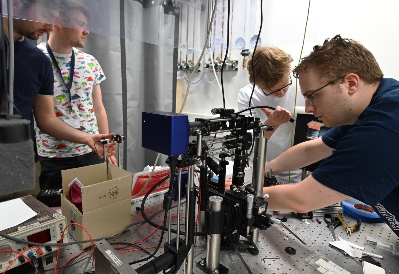 Vier junge Männer arbeiten in einem Labor an einem optischen Aufbau und testen diesen