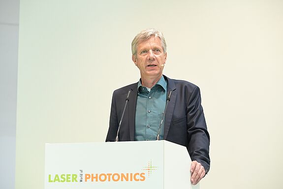 Ein Mann im Anzug steht am Rednerpiult mit der Aufschrift LASER World of PHOTONICS