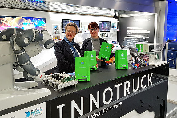 Zwei Frauen mit mehreren handliche grünen Kästen im moderenen Innenraum des InnoTrucks.