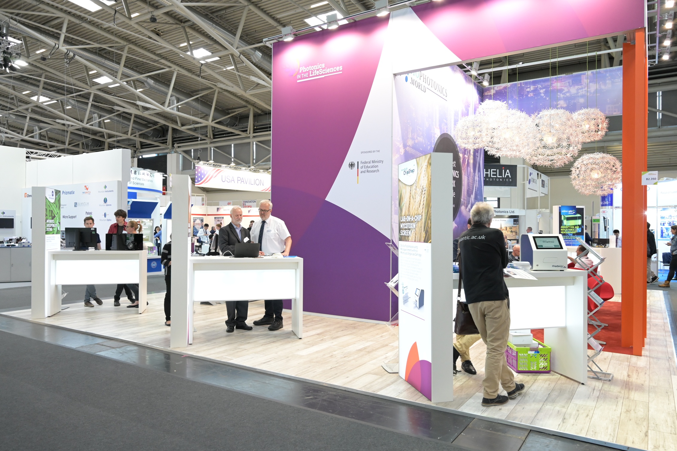 Blick auf einen Messestand mit verschiedenen Ausstellungstischen, Menschen betrachten Exponate und unterhalten sich